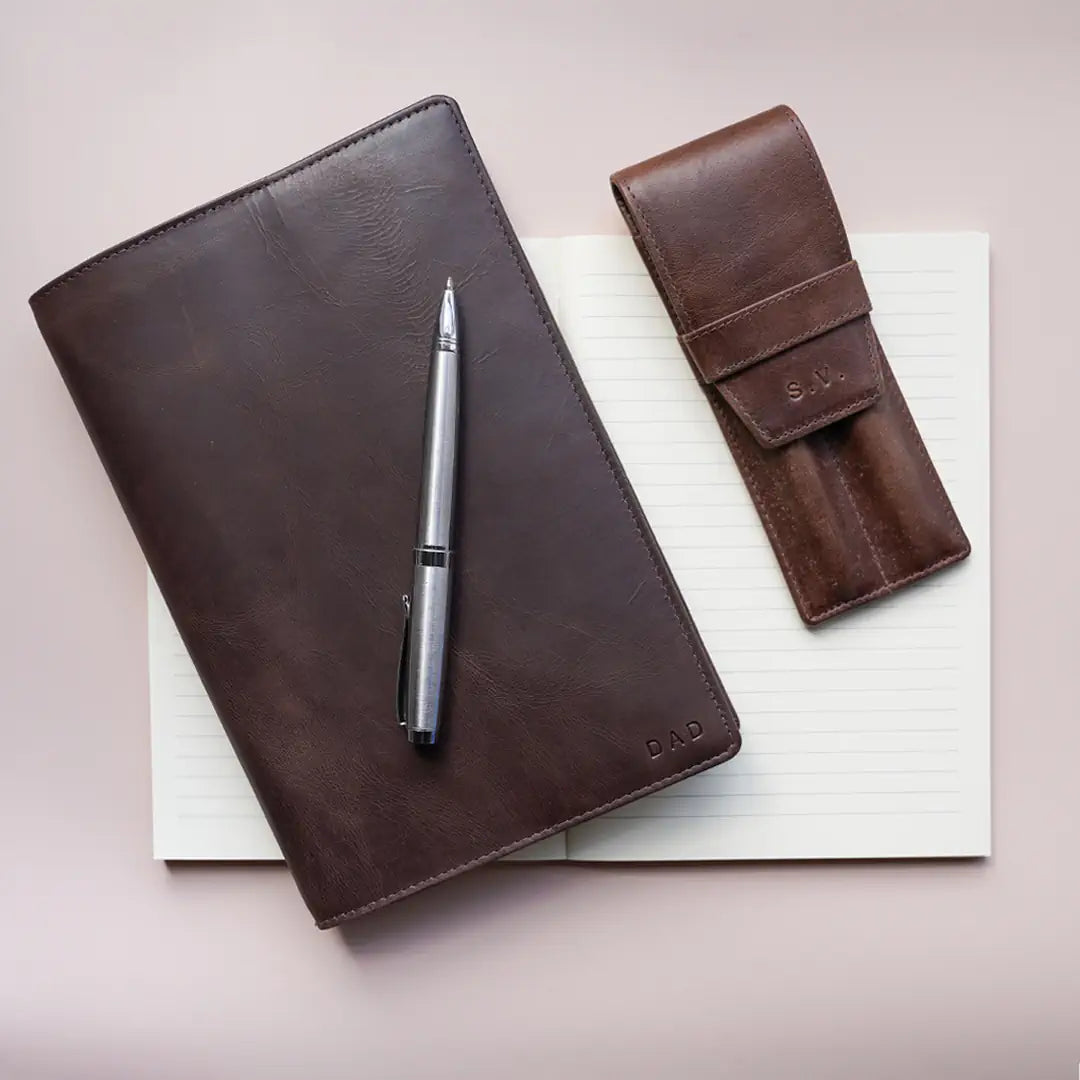 Brown leather notebook, pen, and pencil case on a light surface